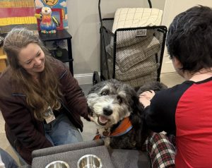 Erica pets Beto, a therapy-trained dog. Ashley Busone Rogriguez, Beto is to their right appreciating the interaction.